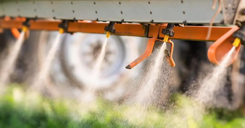 Close up image of a boom sprayer with jets of spray directed towards a crop.